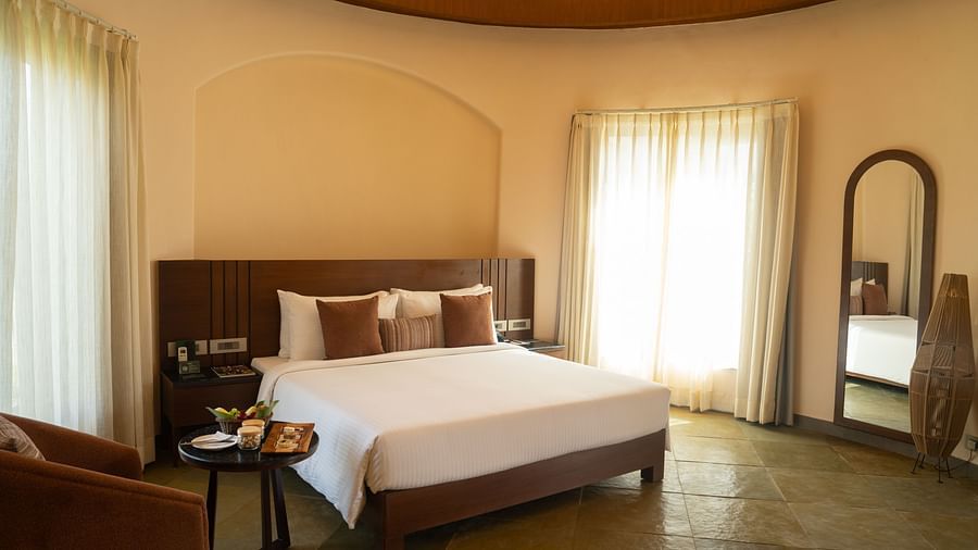 A warm bedroom with a double bed, soft lighting, and full-length mirror near the window at Ananta Spa and Resort, Ajabgarh.