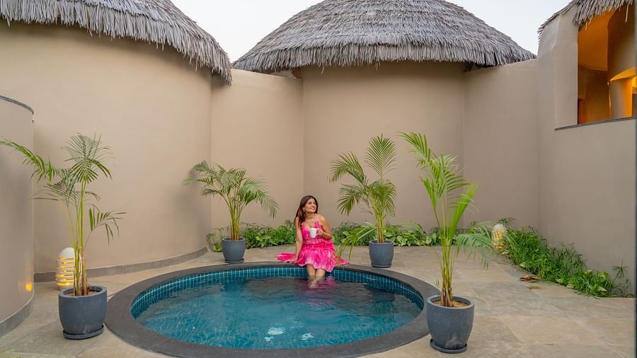 A private plunge pool courtyard with a woman in pink attire, surrounded by thatched-roof cottages at Ananta Spa and Resort, Ajabgarh.