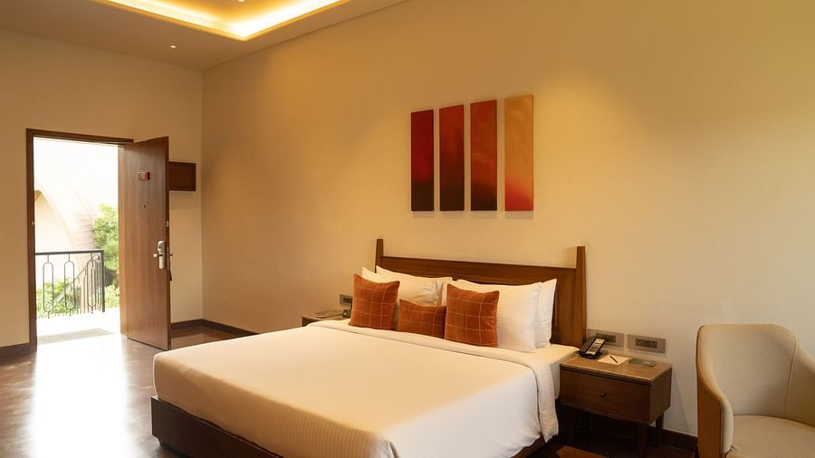 Cosy bedroom with warm lighting, modern artwork, bedside table, a seating area, and outdoor access at Ananta Spa and Resort, Ajabgarh.