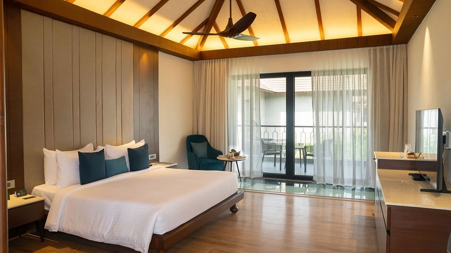 A spacious modern bedroom with a king-size bed, wooden flooring, and a balcony with glass doors at Ananta Spa and Resort, Ajabgarh.