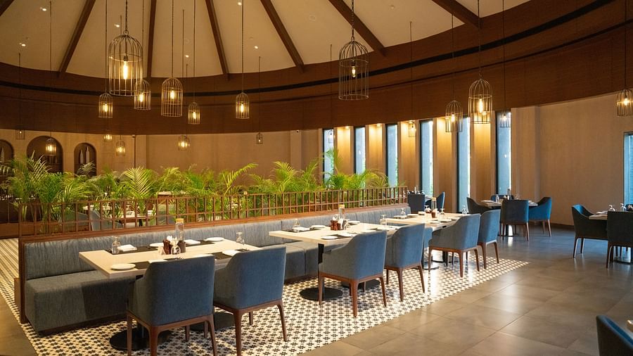 A stylish indoor dining area with blue chairs, round tables, and a high wooden ceiling under warm lighting at Ananta Spa and Resort, Ajabgarh.