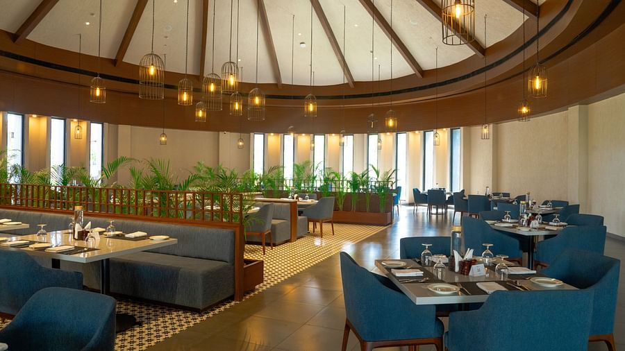 A spacious, elegant dining area with teal chairs, round tables, and a high domed ceiling with natural light at Ananta Spa and Resort, Ajabgarh.