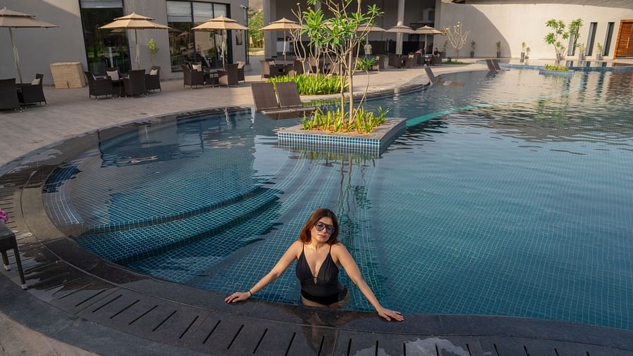 Duplicate of a woman relaxing at the edge of a modern outdoor swimming pool, surrounded by loungers and property at Ananta Spa and Resort, Ajabgarh.