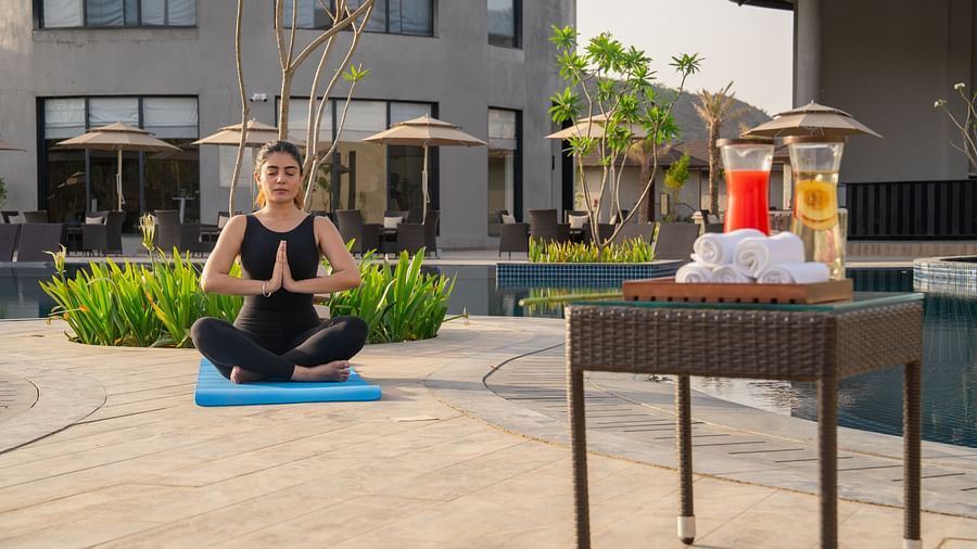 A woman practising yoga near the pool at Ananta Spa and Resort, Ajabgarh with a table of refreshments  besides her