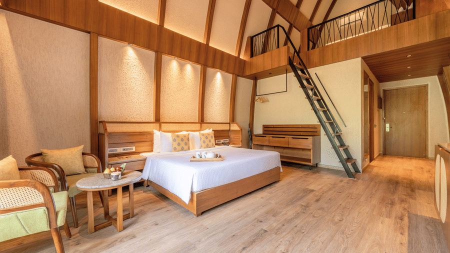 an interior of a bamboo villa with a king size bed and a stairs to the second deck at Ananta Spa and Resort, Ajabgarh