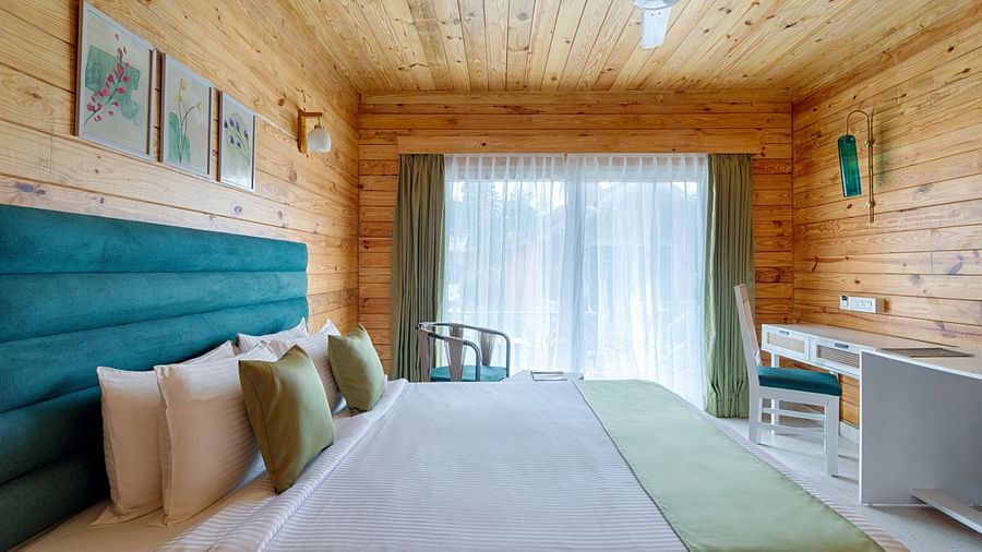 A warm, inviting bedroom featuring a large bed with a teal headboard and sage green accents, flanked by wooden walls and a sheer curtained window Aralea Beach Resort by Stone Wood, Morjim