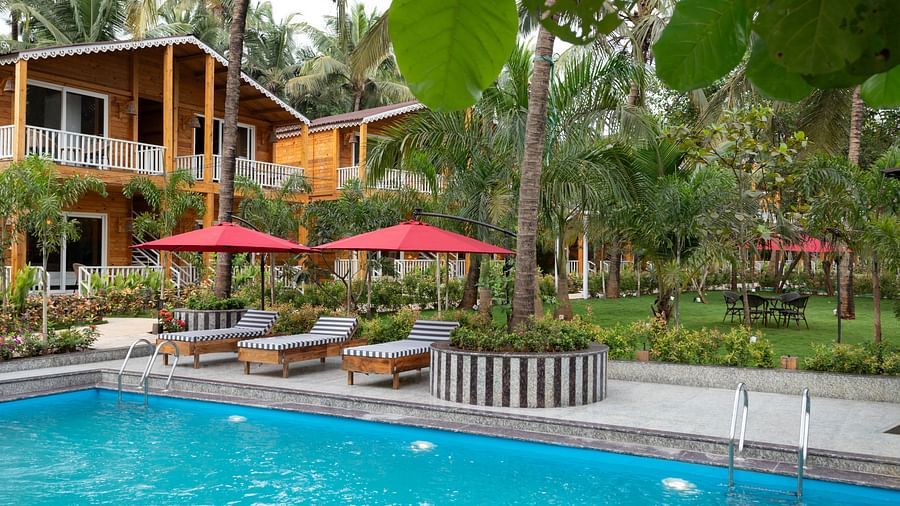 Lush poolside garden view with red umbrellas and tropical wooden cabins Aralea Beach Resort by Stone Wood, Morjim