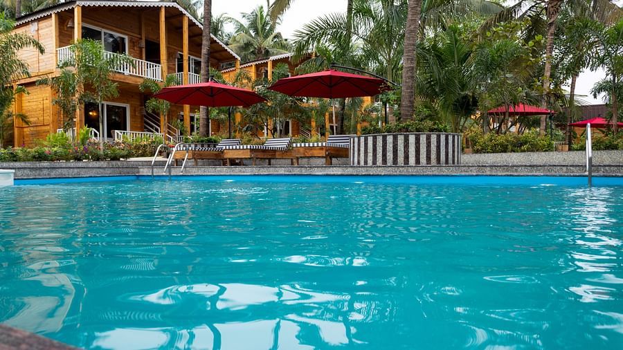 A view across a swimming pool towards two-storey wooden resort cabins with red umbrellas and sun loungers in the foreground - Aralea Beach Resort by Stone Wood, Morjim