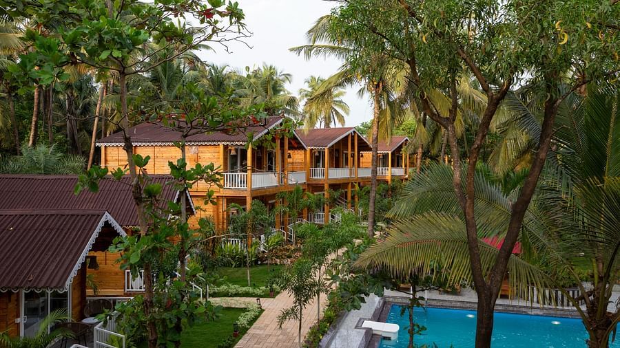 An elevated view of wooden resort cabins amidst lush greenery with a view of the pool and garden pathway - Aralea Beach Resort by Stone Wood, Morjim