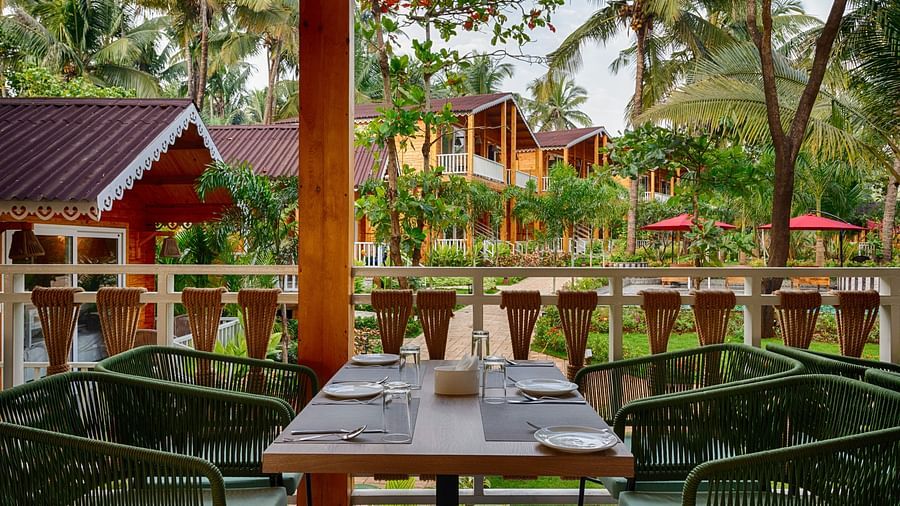 An image of the dining area with four chairs and a table in between and cabins in the background - Aralea Beach Resort by Stone Wood, Morjim