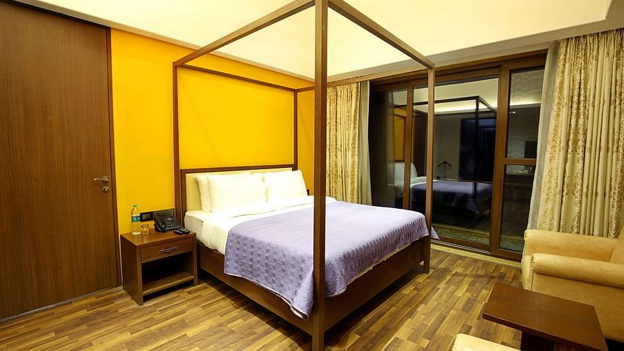 A bedroom with a cosy bed, warm interiors, and a large window draped with long curtains