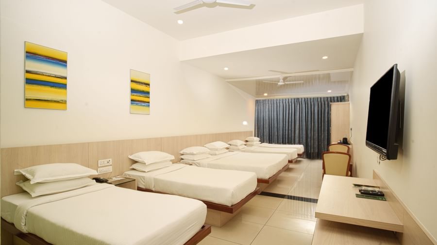 Spacious hotel room featuring four single beds lined up, a wall-mounted TV, and bright artwork at Arawali Ananta Elite, Jaipur.