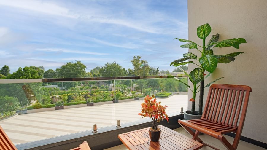 Outdoor balcony with seating, potted plants, and a glass railing overlooking the hotel grounds at Arawali Ananta Elite, Jaipur.