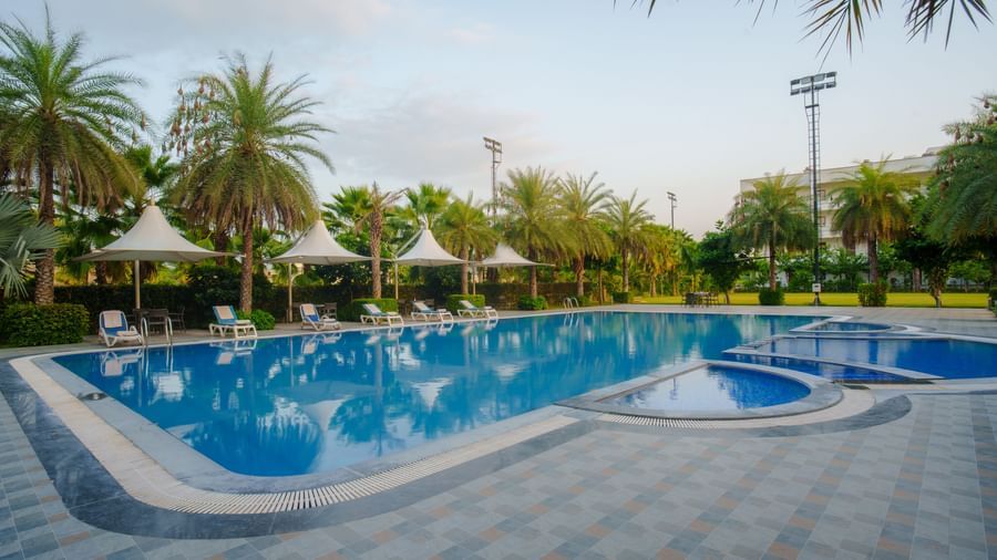 Outdoor swimming pool area with sun loungers and palm trees at Arawali Ananta Elite, Jaipur.