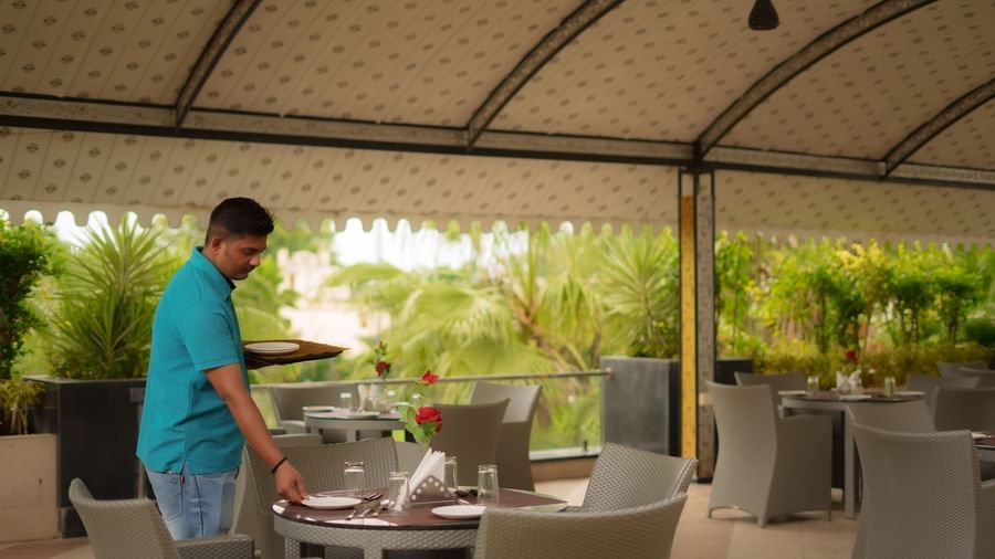 Staff member setting a dining table in the covered outdoor restaurant area at Arawali Ananta Elite, Jaipur.