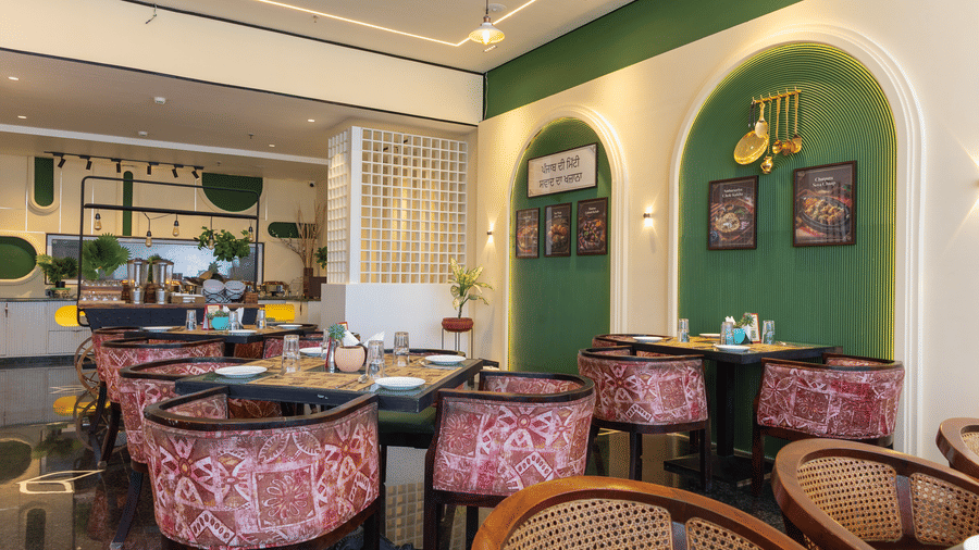 Dining room at Hotel Bawa, Udaipur with square tables, patterned armchairs, green arched wall alcoves, hanging lamps, and background counter space.