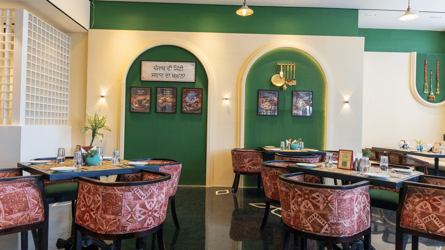 Restaurant dining area at Hotel Bawa, Udaipur featuring square tables, patterned armchairs, arched wall alcoves with pictures, and wall sconces.