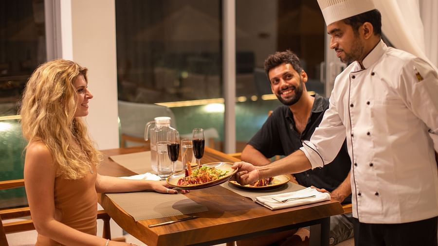 image of a chef serving well decorated plate of a sea food cuinsine to the couple at the the beacon by the bay villas and suites in dondra, sri lanka