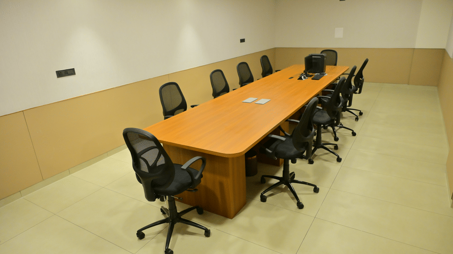 Conference room at Bhavanis Vista By Icon Hosur with a long wooden table, black mesh chairs, and warm-toned walls.