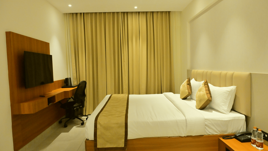 Deluxe room at Bhavanis Vista By Icon Hosur with a king bed, wooden work desk, and gold-toned curtains.