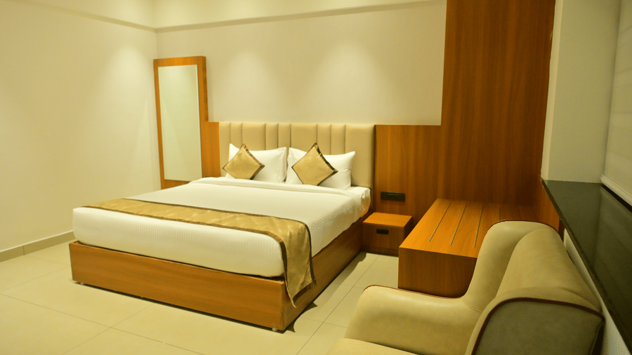 Suite bedroom at Bhavanis Vista By Icon Hosur with a king bed, wooden headboard panel, and a sofa seating area.