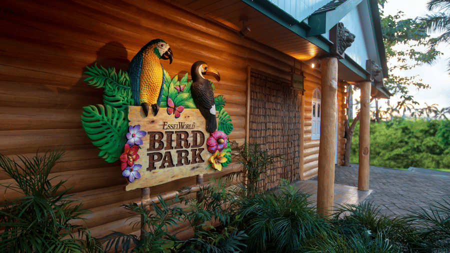 Log cabin building with a sign saying Birds Park and colorful parrot illustrations on the facade.
