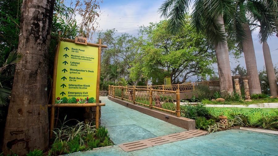 Signpost at a park entrance with lush greenery and a paved pathway leading into the distance.