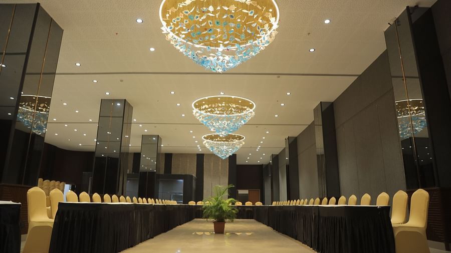 A large, elegant conference room with a long table and chairs under grand chandeliers - Biznotel By Pride Surat