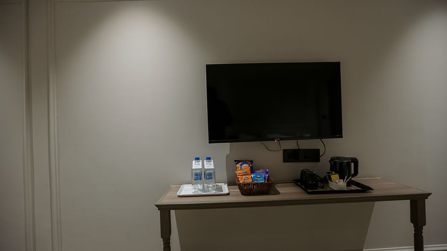A hotel room's television mounted on the wall, with a desk and amenities below - Biznotel By Pride Surat
