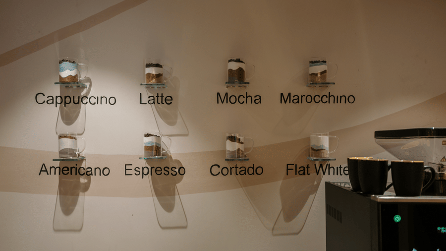 Coffee menu wall display at Biznotel by Pride Surat showing various coffee options alongside cups.