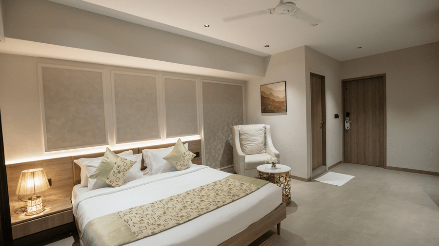 Elegant king guest room at Biznotel by Pride Surat featuring a large bed, ambient headboard lighting, and an armchair seating area.