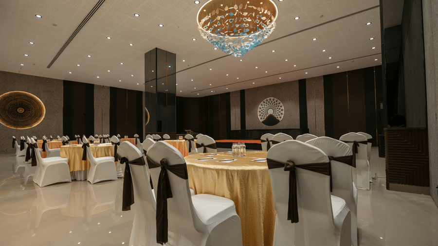 Elegant event venue at Biznotel by Pride Surat with round tables, decorated chairs, and warm chandelier light.