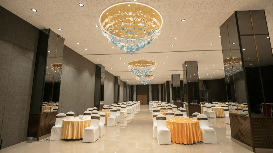 Spacious banquet hall at Biznotel by Pride Surat featuring elegant round table seating and stylish chandeliers.