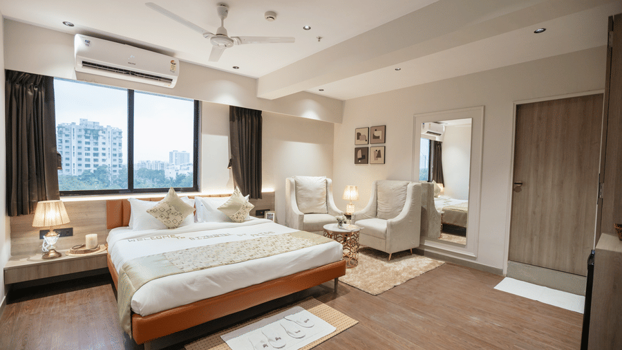 Spacious and modern hotel room at Biznotel by Pride Surat featuring a comfortable bed, large windows, and a seating area.