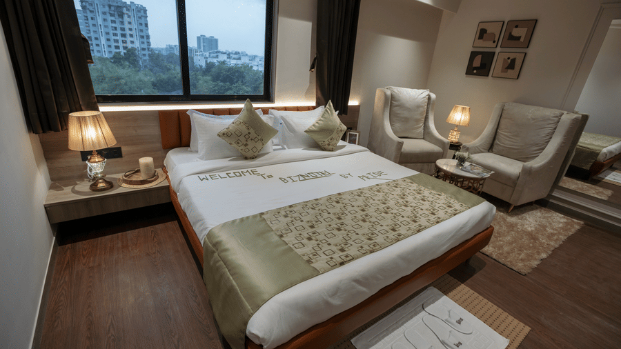 Cosy hotel bedroom at Biznotel by Pride Surat with a large bed, plush armchairs, and city-view window.