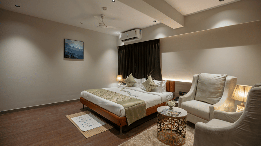 Elegant guest room at Biznotel by Pride Surat featuring a large bed, seating area with armchairs, and warm ambient lighting.