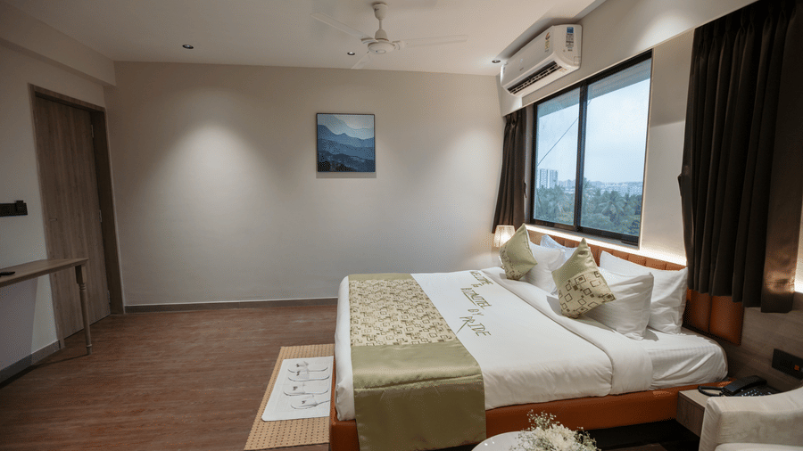 Well-lit guest room at Biznotel by Pride Surat featuring a large bed, wall art, air conditioning, and a window.