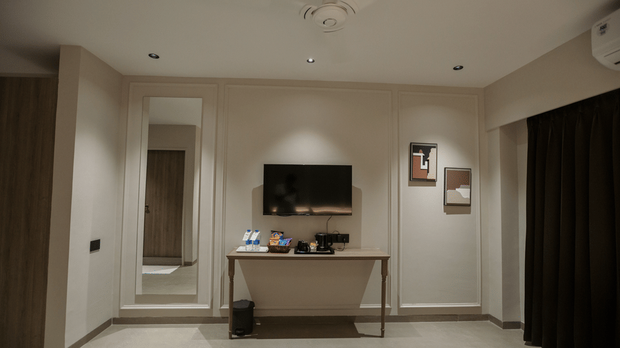 Modern guest room wall layout at Biznotel by Pride Surat featuring a wall-mounted TV, console desk with tea/coffee maker, and a full-length mirror.