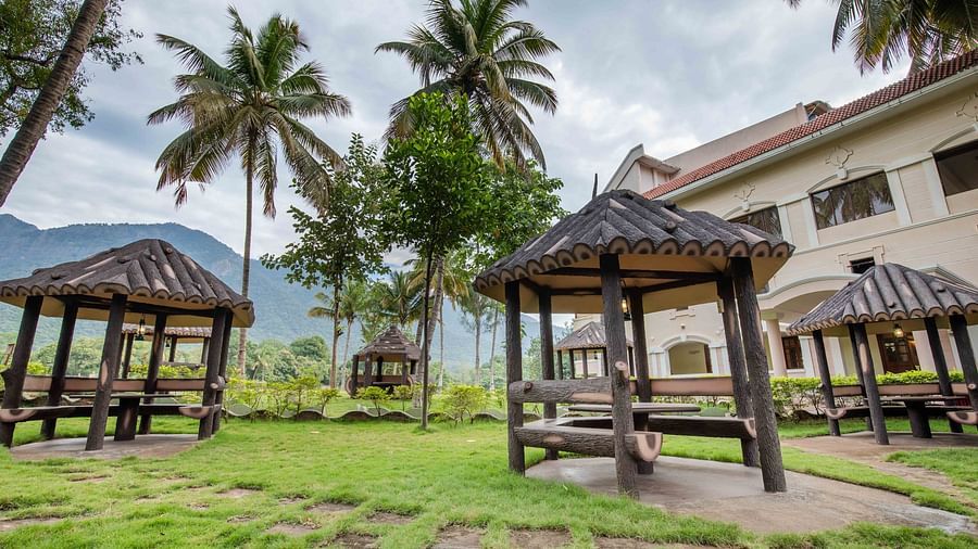 Grassy outdoor area with shaded wooden gazebos, ideal for relaxing, set among coconut trees with a view of the nearby resort - Black Thunder, Coimbatore