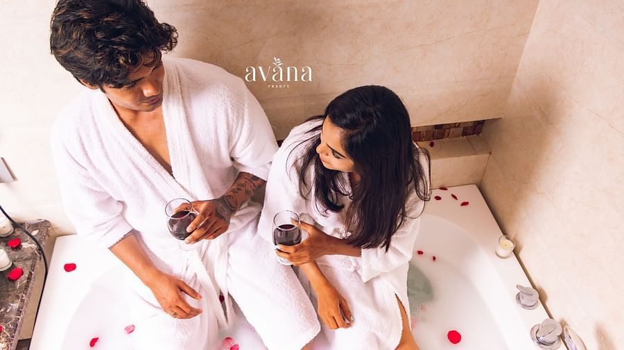 A couple wearing white robes, sitting on a bed and holding hands