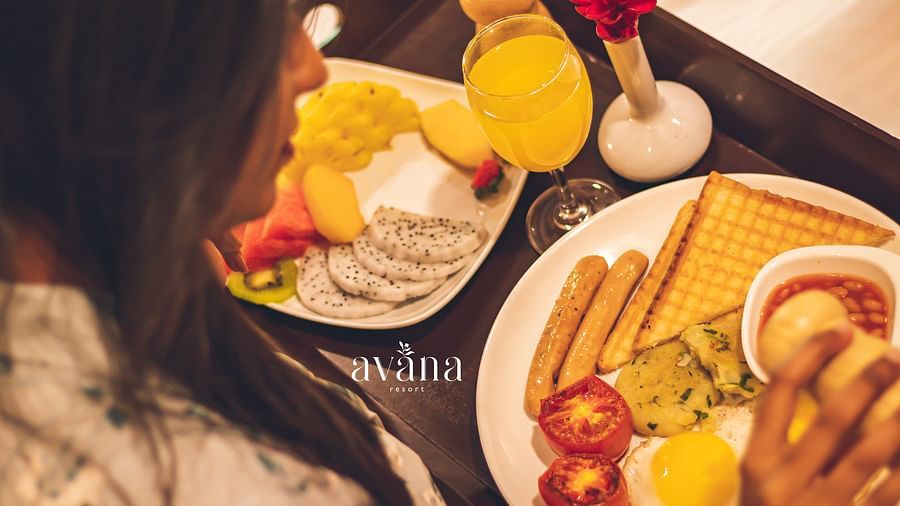 Woman enjoying a cosy breakfast in bed with waffles, fruit, and coffee.