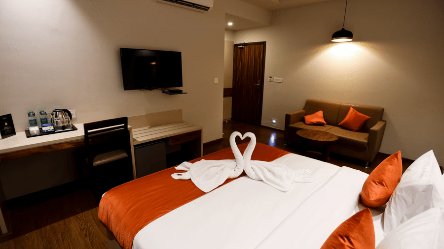 Side view of a room a with a double bed, wall-mounted TV, and a seating area at Amara Grand Baga, Goa.