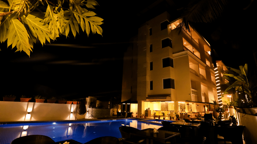 An exterior of a multi-storey building of Amara Grand Baga, Goa, with a swimming pool on the side.