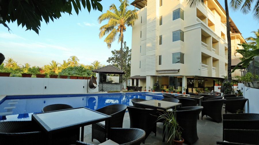 Exterior of Amara Grand Baga, Goa, with chairs and tables by the pool.