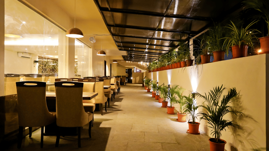Back view of a dining area with tables and chairs and pots of plants beside it at Amara Grand Baga, Goa.