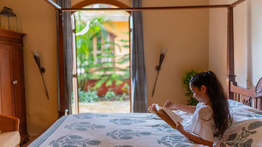 a woman reading a book in bed tucked under a dohar as the door is wide open