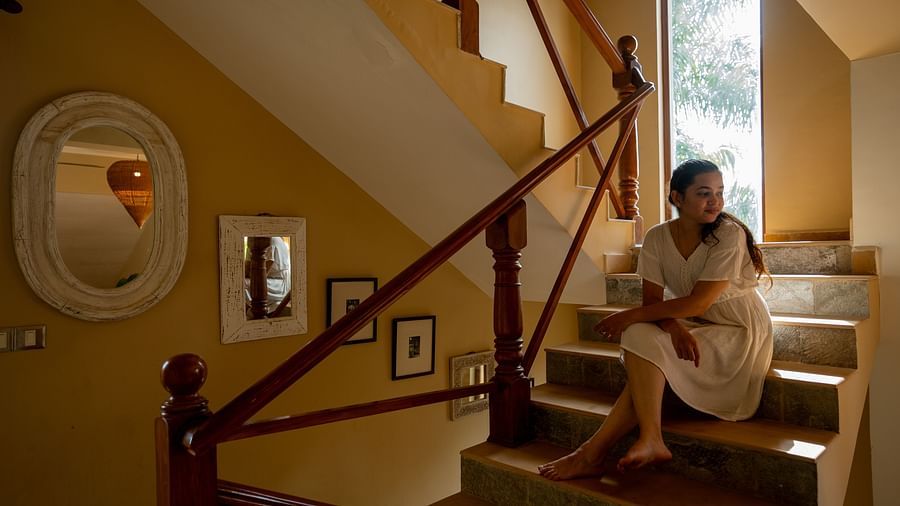 A woman sitting on the staircase looking around and the walls on the staircase have mirrors and showpieces hung