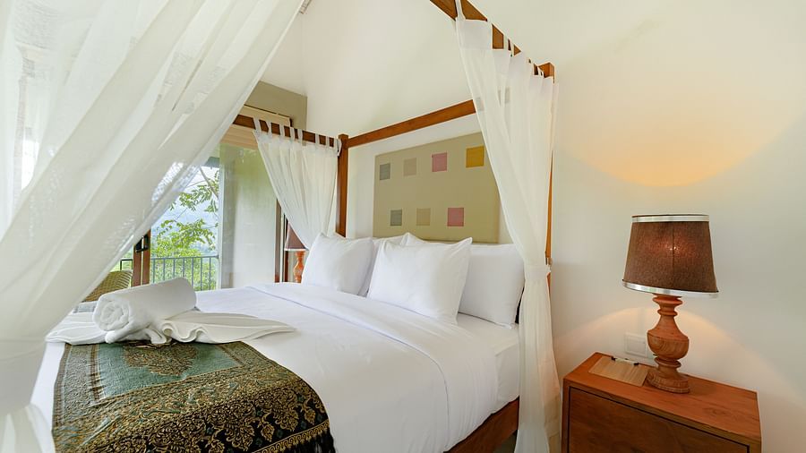 A side view of a canopy bed beside a lamp placed on a table | Celestial Hills - Villas & Suites in Kandy