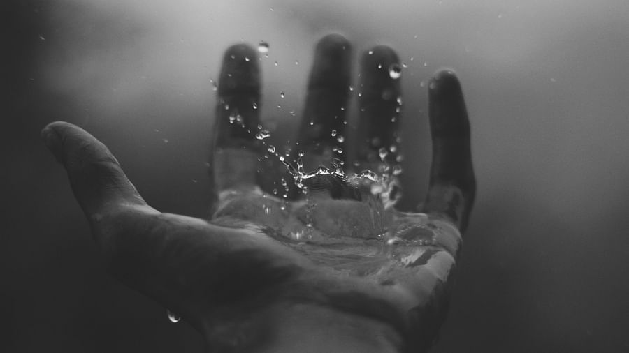 a black and white picture of a person holding out his hand to catch rain drops