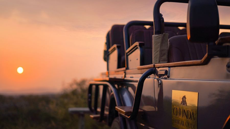 a jeep in the foreground with the sun setting in the background